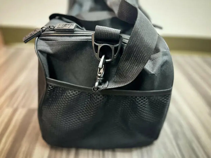 Black duffel bag with a mesh pocket and adjustable strap.