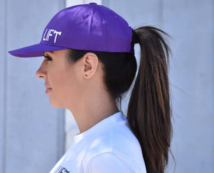 Purple baseball cap with ’LIFT’ text worn by a person with a ponytail.