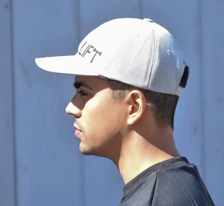 White baseball cap with ’LIFT’ text worn sideways on a person’s head.