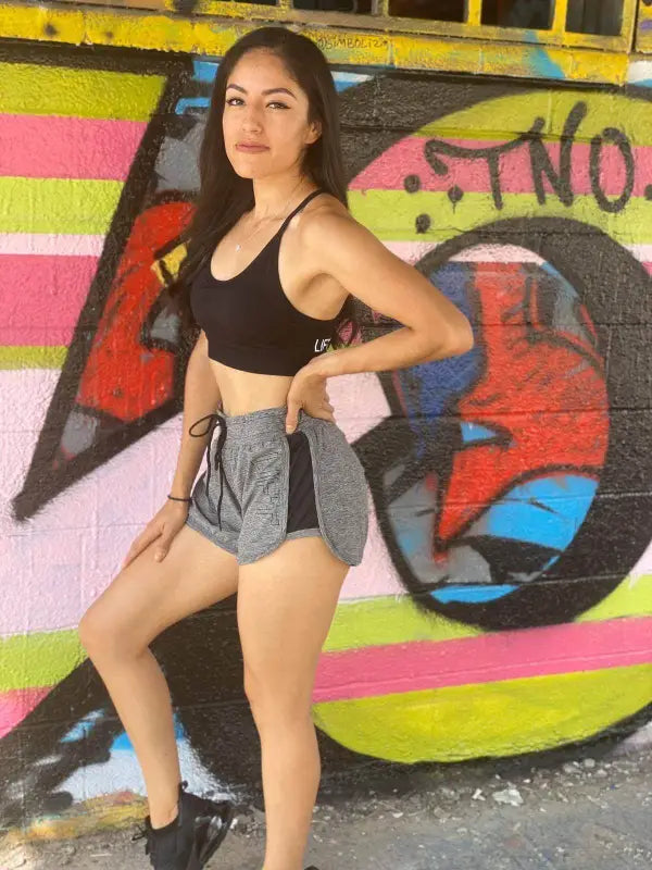 Woman posing in athletic wear against a colorful graffiti wall.
