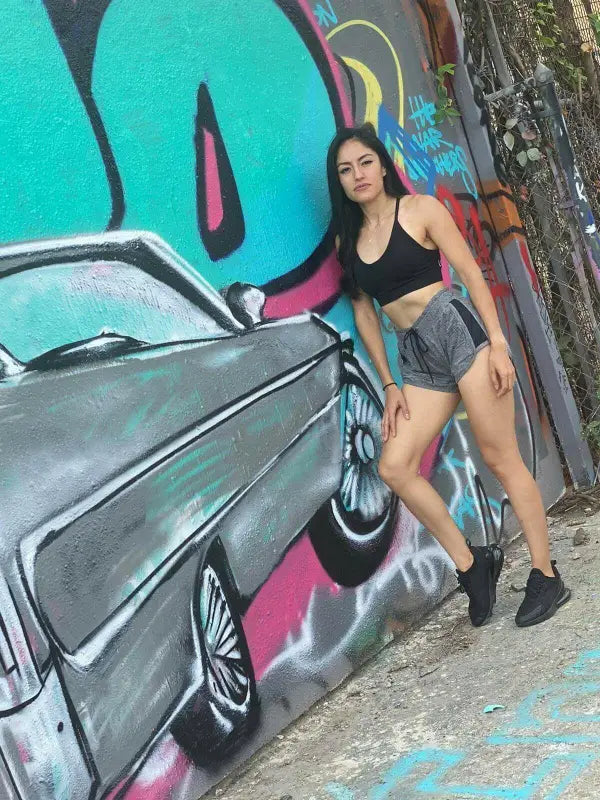 Woman posing next to a colorful graffiti mural depicting a vintage car.