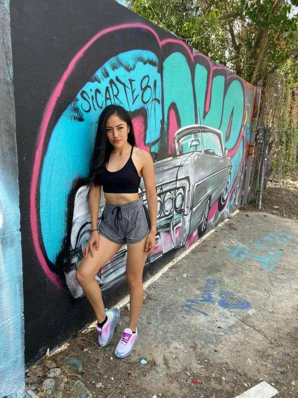 Young woman posing in front of colorful graffiti wall featuring a car design.