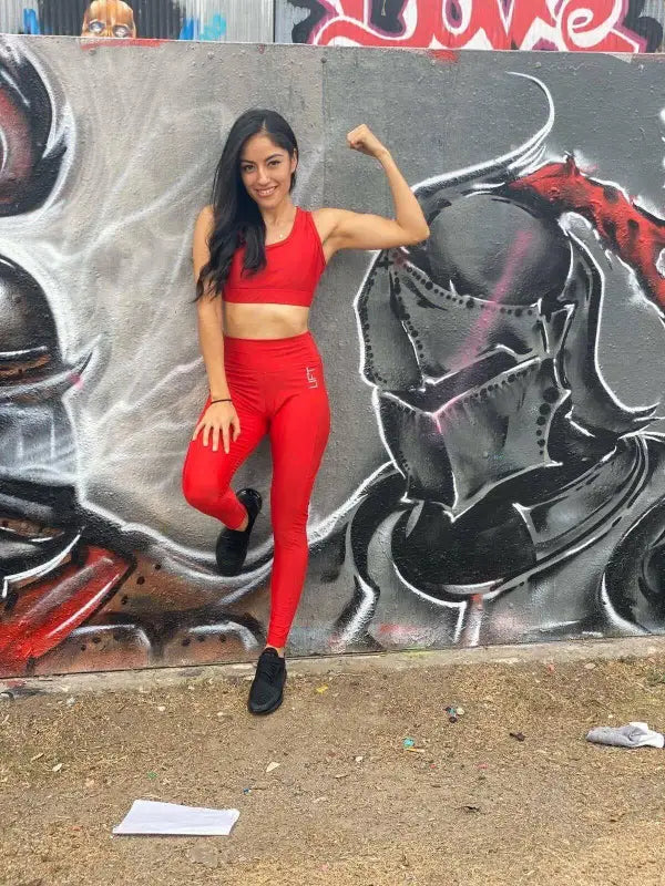 Woman in a bright red workout outfit posing in front of a graffiti wall.