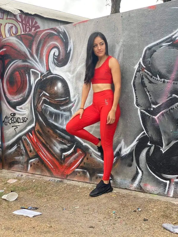 Woman in a bright red workout outfit posing against a graffiti wall.