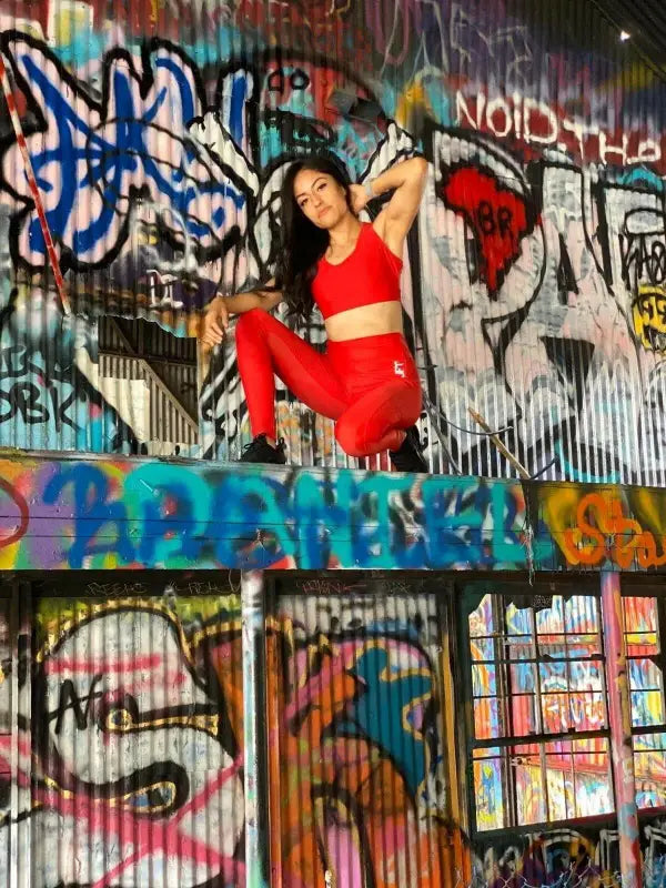 Woman in a bright red outfit posing against a graffiti-covered wall.