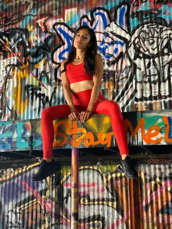 Woman in a bright red outfit sitting on a surface against a graffiti-covered wall.