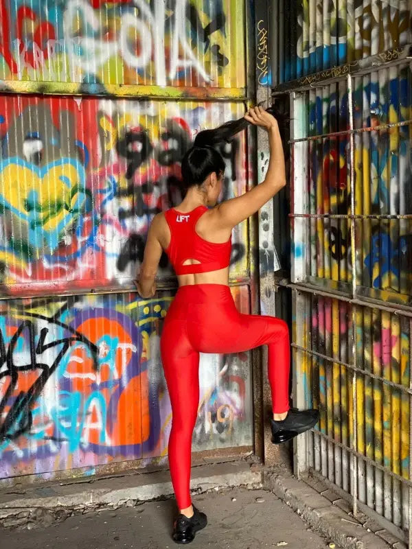Woman in a bright red athletic outfit posing against a graffiti-covered wall.