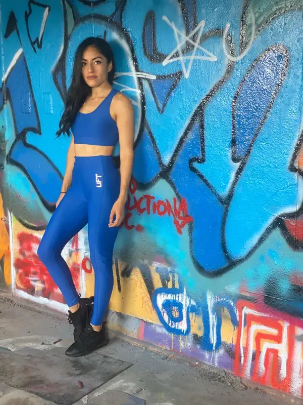 Woman in blue athletic wear posing against a graffiti wall.