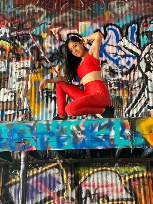 Woman in a red outfit posing against a graffiti-covered wall.