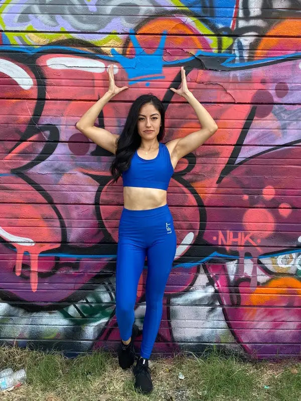 Woman in blue athletic wear posing against a colorful graffiti wall.