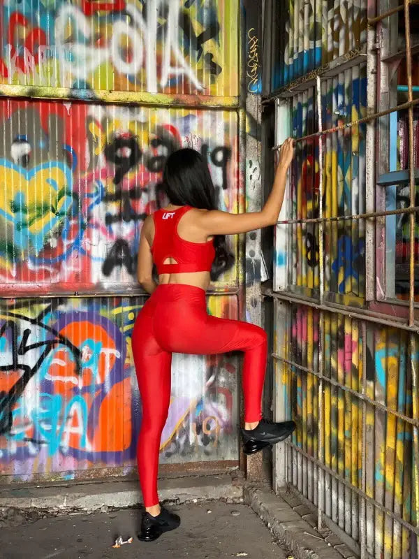 Woman in bright red athletic wear posing against a graffiti-covered wall.