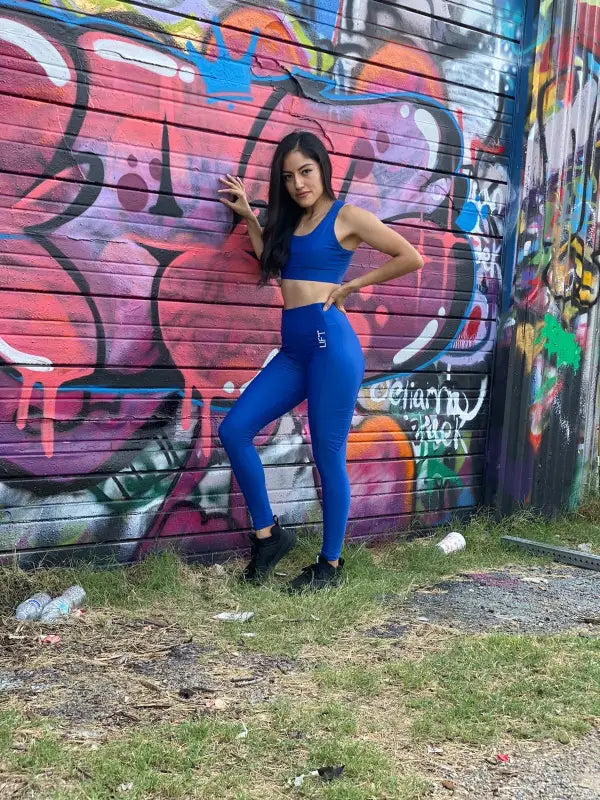 Woman in blue athletic wear posing in front of a graffiti wall.