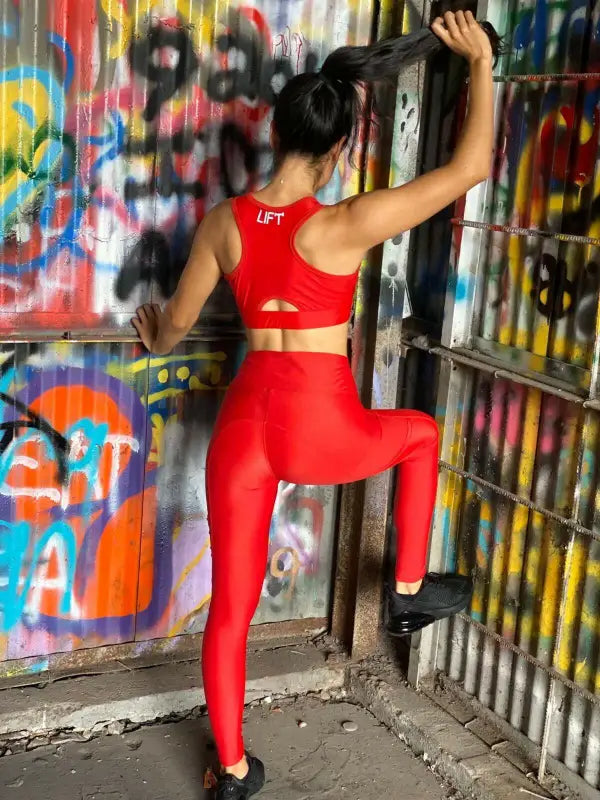 Woman in a bright red workout outfit posing against a graffiti-covered wall.