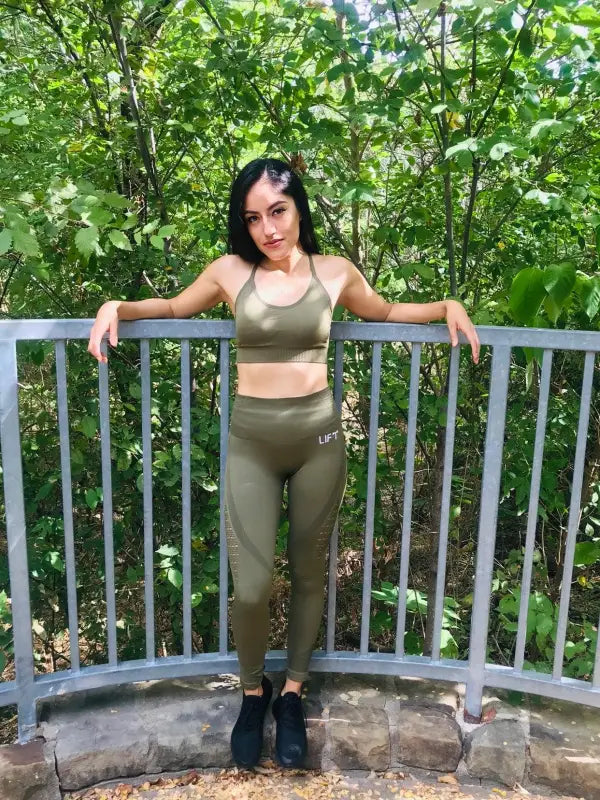 Woman in olive green athletic wear posing on a balcony railing.