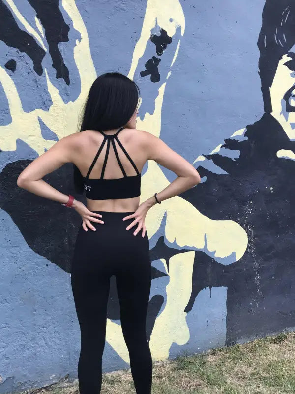 Woman in black athletic wear standing with hands on hips facing a mural.